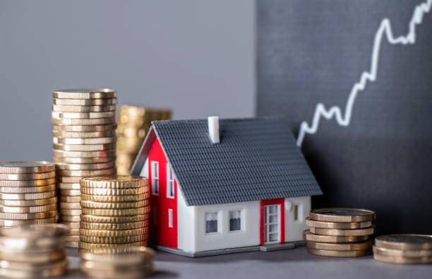 Model house surrounded by stacks of coins with a rising graph in the background.