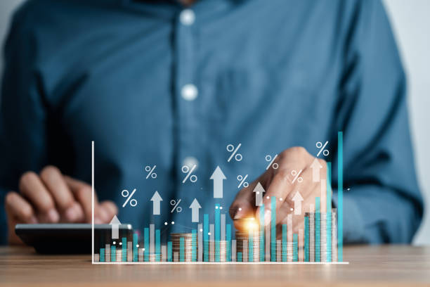 A person in a blue shirt using a calculator with a graphical representation of financial growth and percentages superimposed over stacks of coins