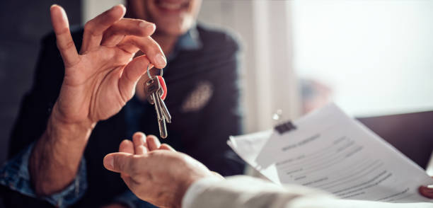 A person hands over a set of keys to another individual who holds paperwork.