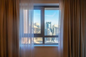 View of Dubai's skyline with modern buildings from an apartment window framed by curtains.