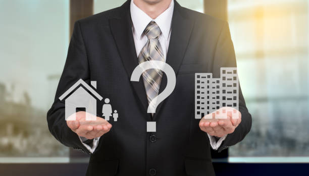 A man in a suit holds a house icon and an apartment building icon with a question mark between them.