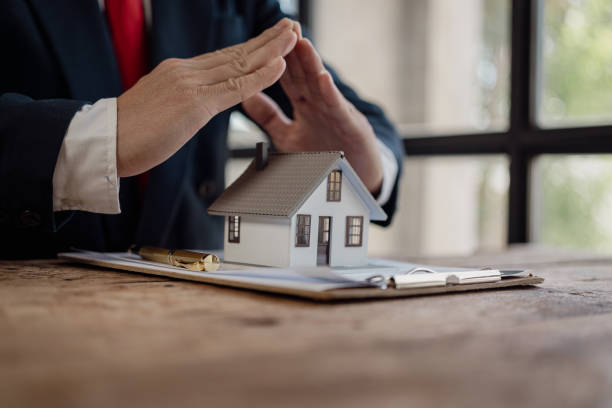 A person in a suit places their hands over a small house model on a clipboard.