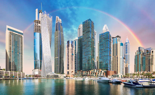 Skyline view of Binghatti Hills featuring modern high-rise buildings, with a rainbow arching in the background.